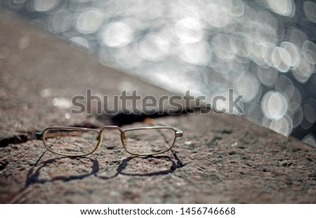 Gold glasses lying on the granite parapet of the river in St. Petersburg with a blurred background of water, highlights and bokeh. Backlighting.