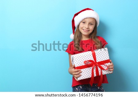 cute cheerful girl in a Christmas hat on a colored background holding a gift
