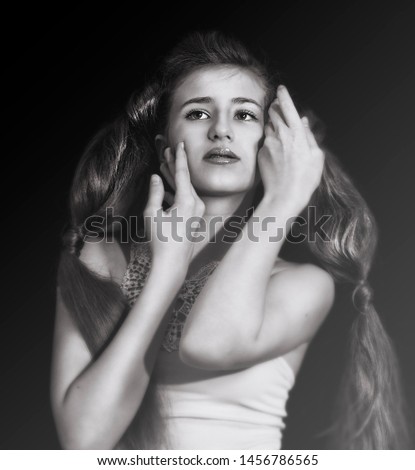 Black-white portrait of a beautiful teen girl with long hair posing, hands near face