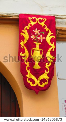 Red and gold embroidered banner hanging on church wall in Andalusian village sunshine