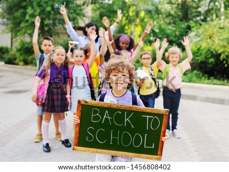 little schoolboy with curly hair on the background of a group of children classmates holding a sign with the inscription "back to school."