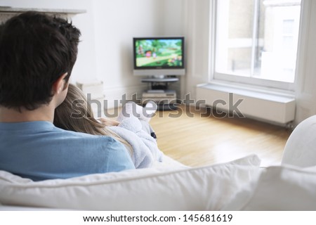 Closeup rear view of father and daughter watching cartoons in television at home
