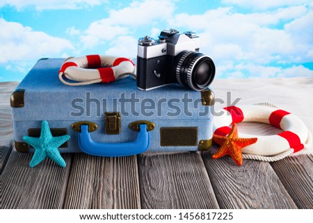 Summer holiday bag concept - suitcase, photo camera and lifebuoy on wooden table and beach