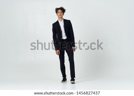 young man in a classic suit on a light background in full growth and curly hair                           