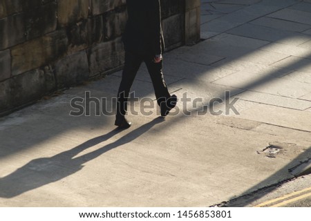 A man in a suit walking on the pavement against the sun with his shadow project behind him