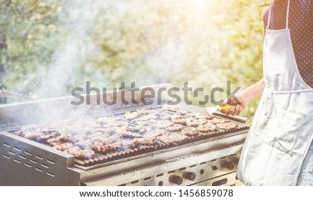 Man cooking meat at dinner barbecue outside of food track - Chef grilling meat in park outdoor - Concept of eating bbq outdoor during summer time - Focus on male hand