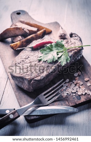 Grilled beef steak on wooden board. Hot meet with vegetables and spices. Retro stylization, vintage film filter