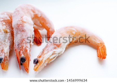 three frozen unpeeled shrimp on a white background