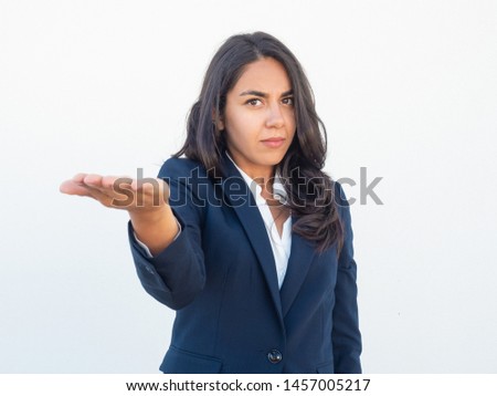 Serious businesswoman showing empty copy space with arm. Young Latin woman in office suit outstretching hand like holding something on palm. Advertising concept