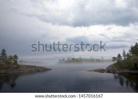 The bay, surrounded on two sides, rocky shores. In the distance, through heavy fog, you can see the neighboring island and access to the lake. Lead heavy sky.