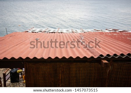 View from above of a red metal roof on a house beside the ocean