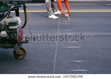 Part of road worker using measuring tape to make lines for pedestrian crosswalk painting on asphalt road surface in the city, selective 