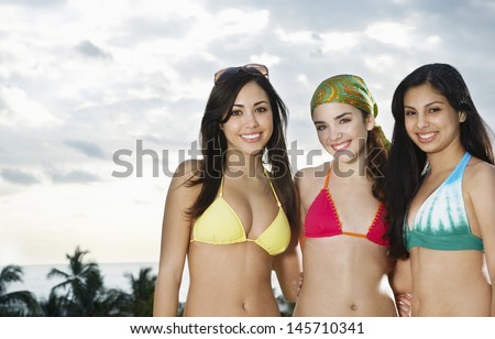 Portrait of beautiful three teenage girls in bikinis against cloudy sky