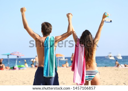 Back view portrait of excited couple celebrating vacation on the beach
