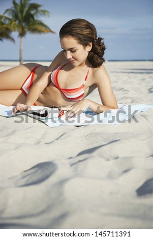 Teenage girl in bikini reading magazine on beach