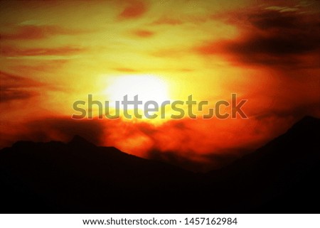 A fiery orange picture of the sun and its rays reflected in the clouds gives an inspiring energetic feel. Silhouette of Himalayan mountain peaks in the background.