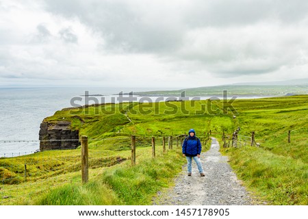 Coastal hiking trail from Doolin towards the Cliffs of Moher, Irish countryside and sea in the background, woman standing looking at camera, Wild Atlantic Way, rainy day in County Clare, Ireland
