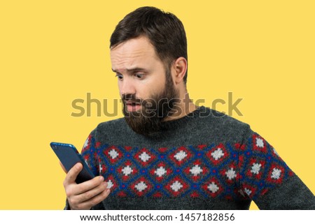Portrait of a guy in a sweater looking emotionally into a mobile phone. Human emotion, reaction, expression, scared emotion