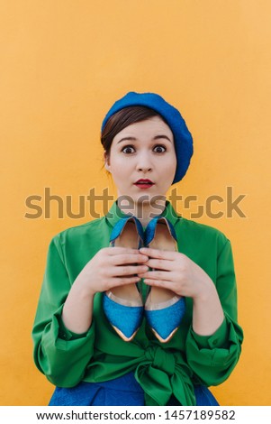 The concept of fashionable summer, blue and green colors. Stylish woman in a blue beret and a green shirt is standing against the orange wall with blue shoes and various emotions