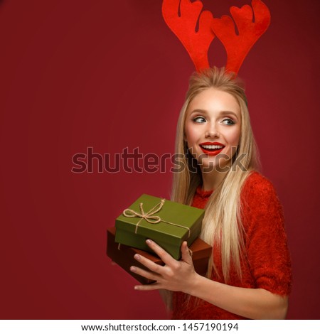 Beautiful blonde girl in a New Year's image with boxes of gifts in hands and deer horns on her head. Beauty face with festive makeup. Photo taken in the studio.