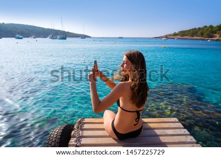Ibiza girl taking smartphone photos at Portinatx beach  pier in Balearic Islands