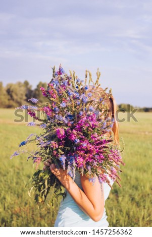 The girl covered her face with a huge bright bouquet of wild flowers. The girl on the background of the field.