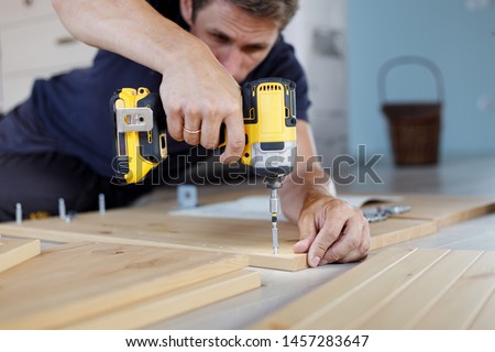 Man assembling furniture at home using a cordless screwdriver Royalty-Free Stock Photo #1457283647