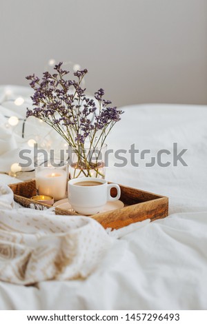 Wooden tray of coffee and candles with flowers on bed. White bedding sheets with striped blanket and pillow. Breakfast in bed. Hygge concept. Royalty-Free Stock Photo #1457296493