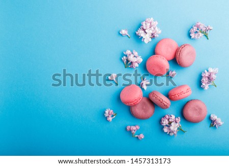 Purple and pink macaron or macaroon cakes with lilac flowers on pastel blue background. Morninig, spring, fashion composition. Flat lay, top view, copy space.