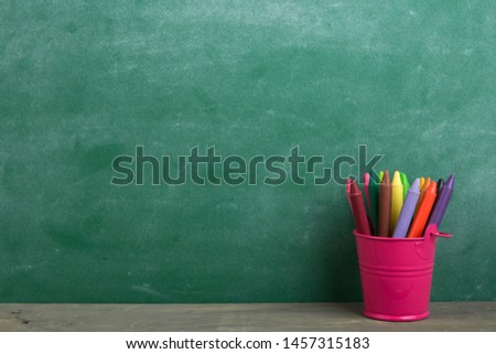colored crayons and toy bear on the wooden table - elementary school education concept, chalkboard background