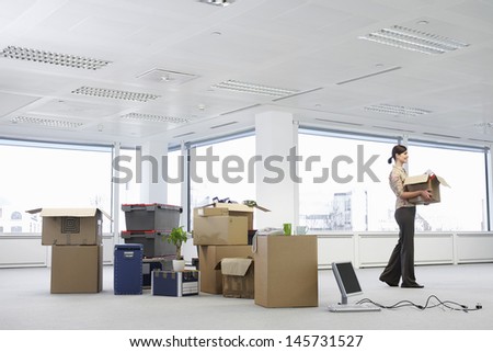 Young businesswoman carrying cardboard box near cartons and equipment in empty office space Royalty-Free Stock Photo #145731527