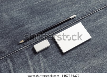 Photo of blank white name card, pencil and eraser on denim background. Copy space for text.