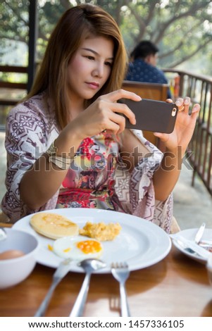 Young woman eating breakfast at restaurant.
Asian girl having food in morning using smart mobile phone taking photo on table.