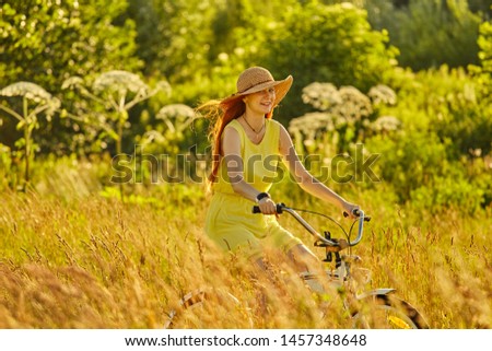 happy red hair girl cyclist in hat biking at sunny meadow