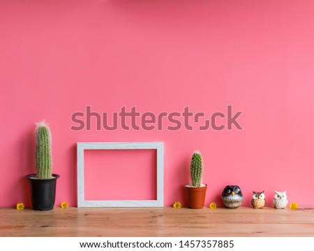 Beautiful  cactus,wooden  picture  frame  and  simulated  owl  on  wood  table  with  pink  background