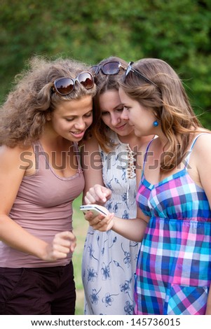 Three young ladies looking and laughing with smart phone