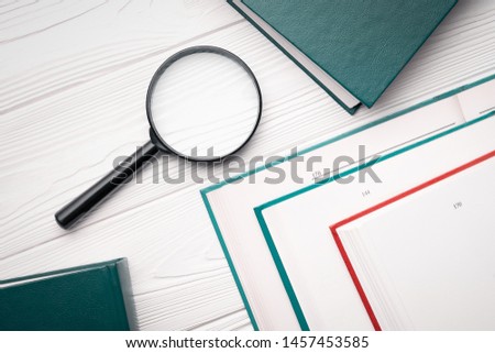 Top view magnifying glass and books opened and closed on a white wooden table.