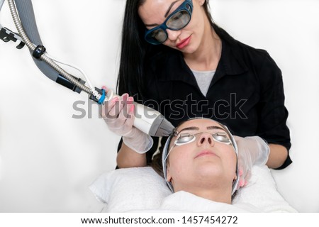 Beautician using a cosmetic laser on a woman's face for facial rejuvenation to smooth skin, on a white background in a medical spa. Royalty-Free Stock Photo #1457454272