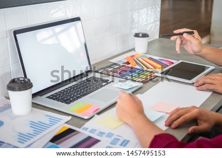 Teamwork of creative designers working on new project and choose color swatch samples for selection coloring on digital graphic tablet with work tools and equipment at workplace.