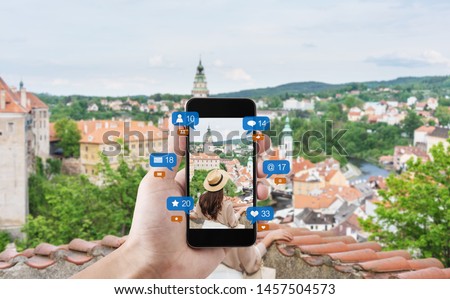 Hand using mobile smart phone taking photo of woman traveling in Cesky krumlov, Czech Republic, with social media and social network notification icons