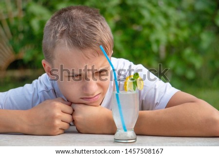 Teenager boy hate fresh organic healthy drink with lemon and mint. Young man drinks natural cocktail outdoors and wrinkles.