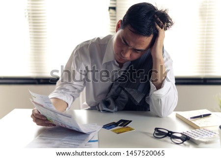 Stressed young Asian man with business office wear holding bills and another hand on head, thinking about  finding money to pay credit card debt and all bills. Financial problem concept. Royalty-Free Stock Photo #1457520065