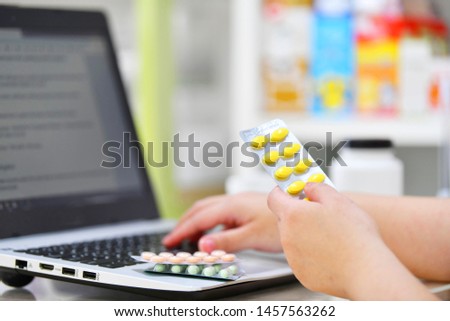 Pharmacist using the computer laptop in chemist shop or pharmacy drug store. Hand holding medicine pack and key the prescription order.