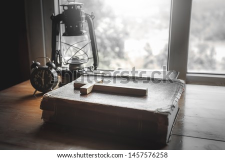 Close up wooden cross with old holy Bible and alarm clock on wooden table in the morning. christian concept.