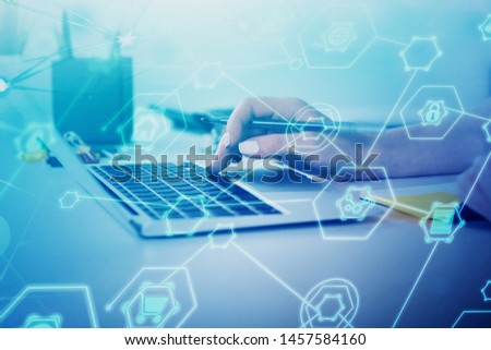 Hands of businesswoman using laptop at office table with double exposure of internet icons. Concept of hi tech in business. Toned image
