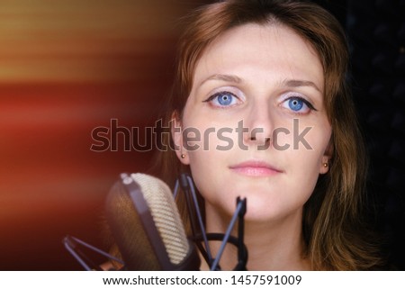 Professional recording vocalist in the Studio, copy space. Beautiful girl singing into the silver microphone. Young woman with black microphone in the recording studio.
