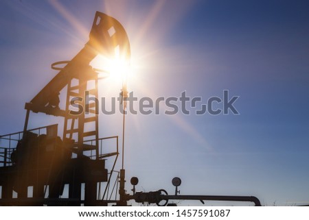 Working oil pump silhouette against sun and blue sky.