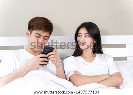 young wife sitting on bed with feeling upset her husband use smartphone in napping time, trouble Asian couple concept