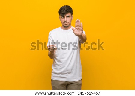 Young hispanic man holding an airplane icon standing with outstretched hand showing stop sign, preventing you.