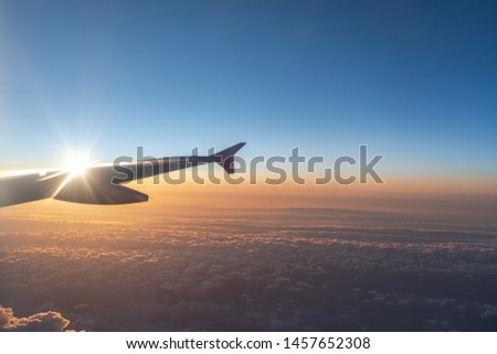 Up in the air, view of aircraft wing silhouette with dark blue sky horizon and cloud background in sun rise time, viewed from airplane window Royalty-Free Stock Photo #1457652308